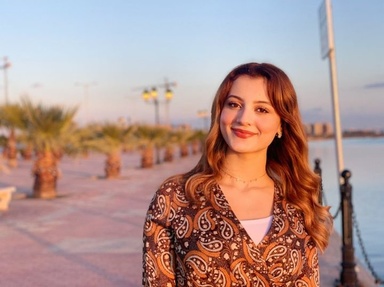 headshot of Aseel Nasr with short palm trees in background on left and bod of water on right